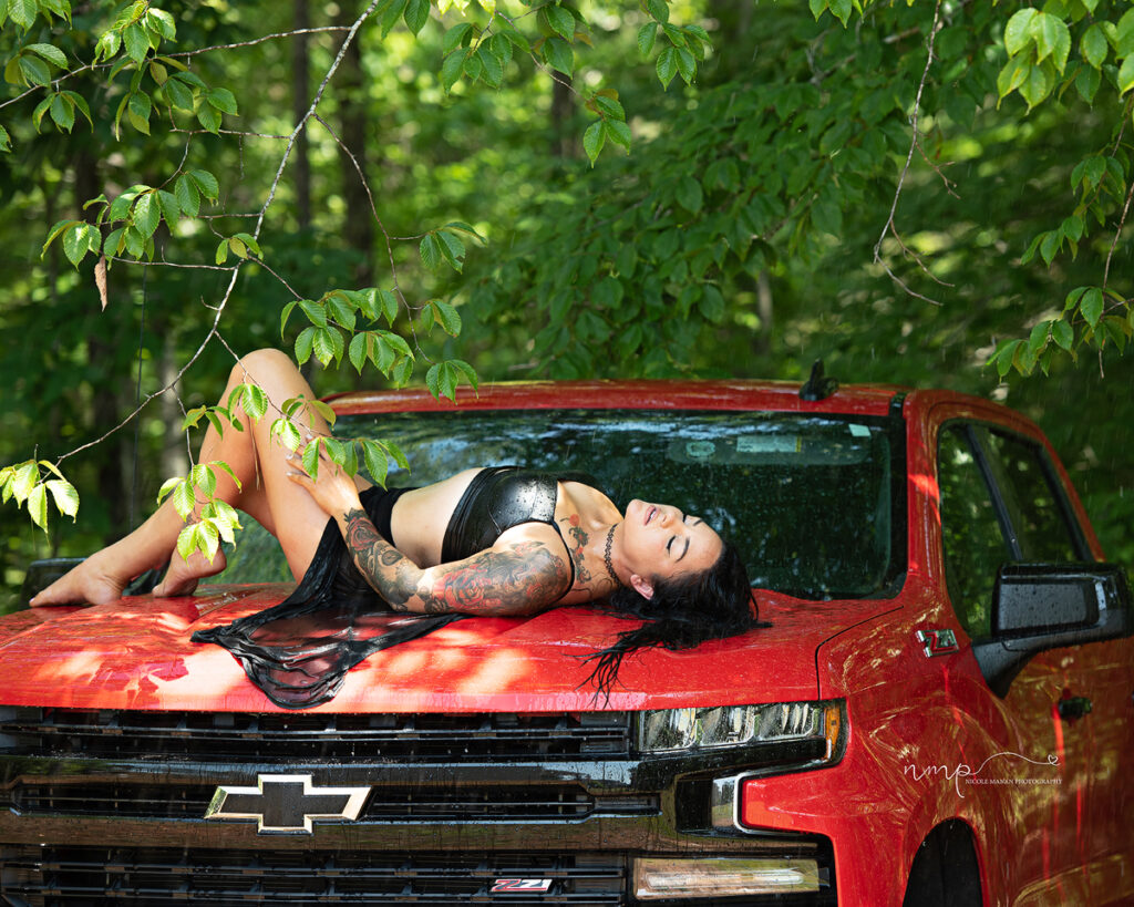 A woman lying on her red truck in the rain in black lingerie during her Columbus GA boudoir session