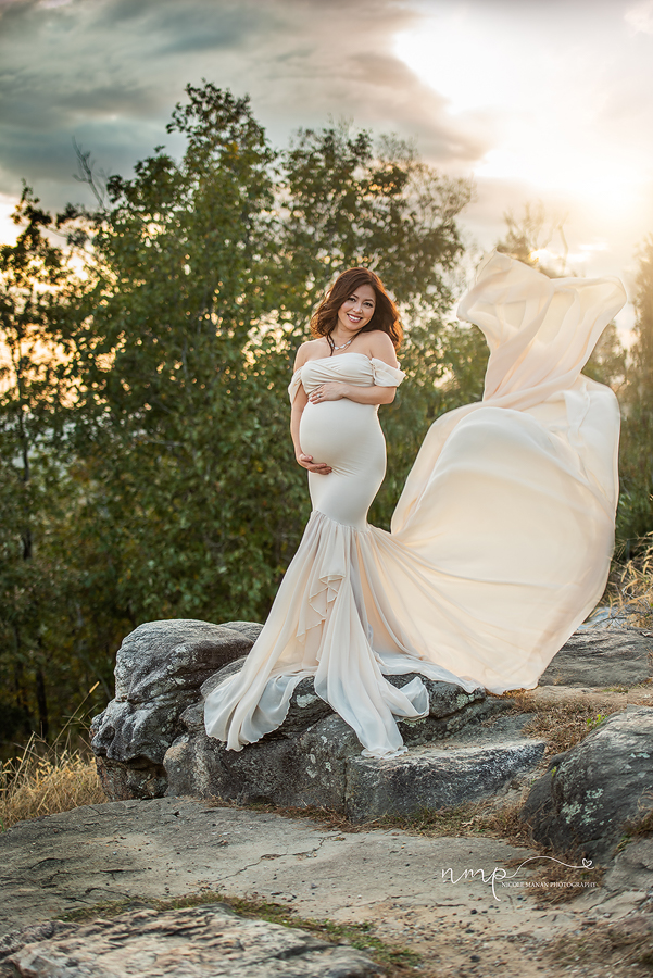 A pregnant woman in beautiful white dress with a flowy tossing train standing on a rock during her Pine Mountain session.