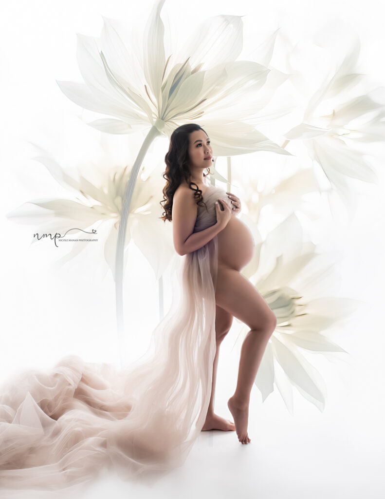 Pregnant woman in a sheer tulle scarf standing in front of a white backlit wall with large flowers
