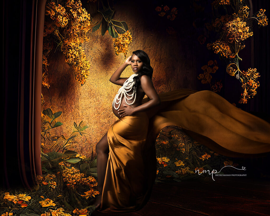 Pregnant woman wearing pearls and a golden fabric standing in front of a yellow wall with lot of yellow flowers