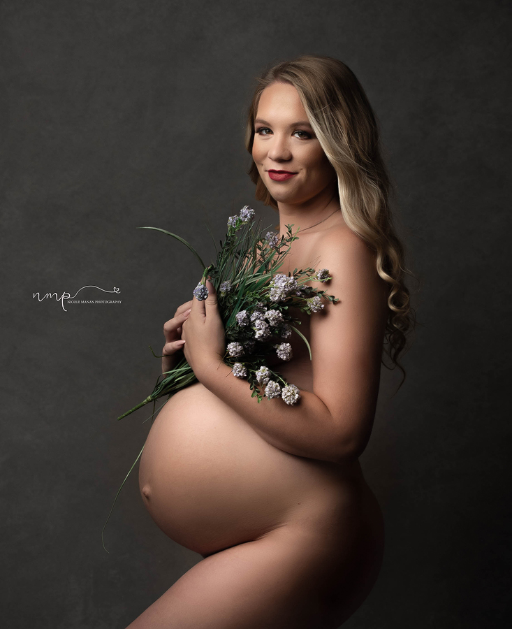 Nude pregnant woman holding purple flowers in front of her during her studio session in Columbus GA