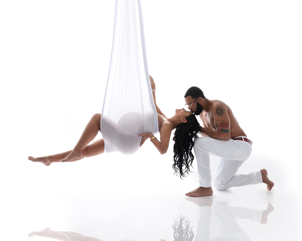 hanging maternity pose with a couple, the man is cradling the pregnant woman's head in this hand and kissing her.