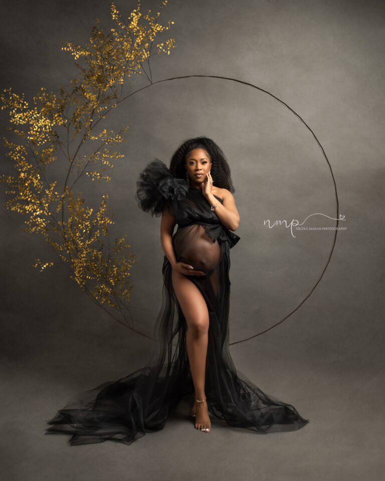 Pregnant woman in a black sheer dress in front of golden flowers during her Columbus Ga maternity session